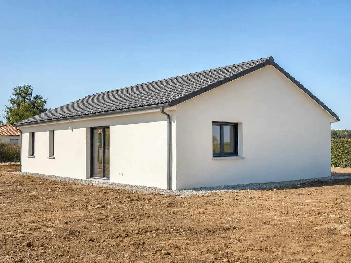 Maison neuve de plain-pied enduite d’un crépi blanc cassé, toit de tuiles grises, bande de gravier au pied des murs