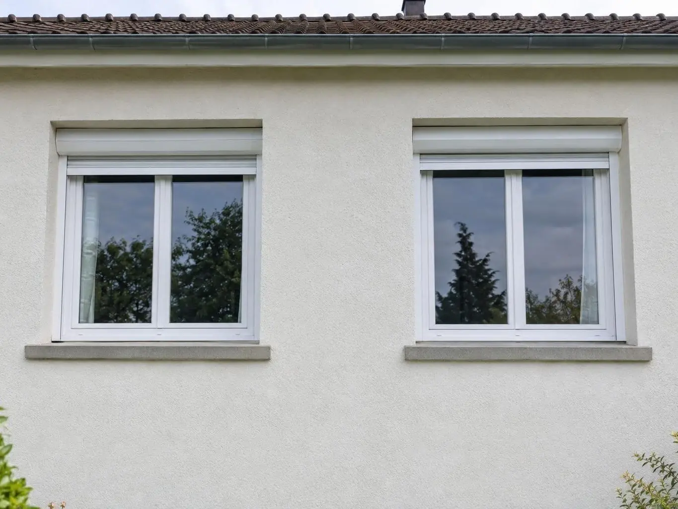 Façade en crépi blanc cassé propre et uniforme sous deux fenêtres blanches à volet roulant et leurs appuis gris clair