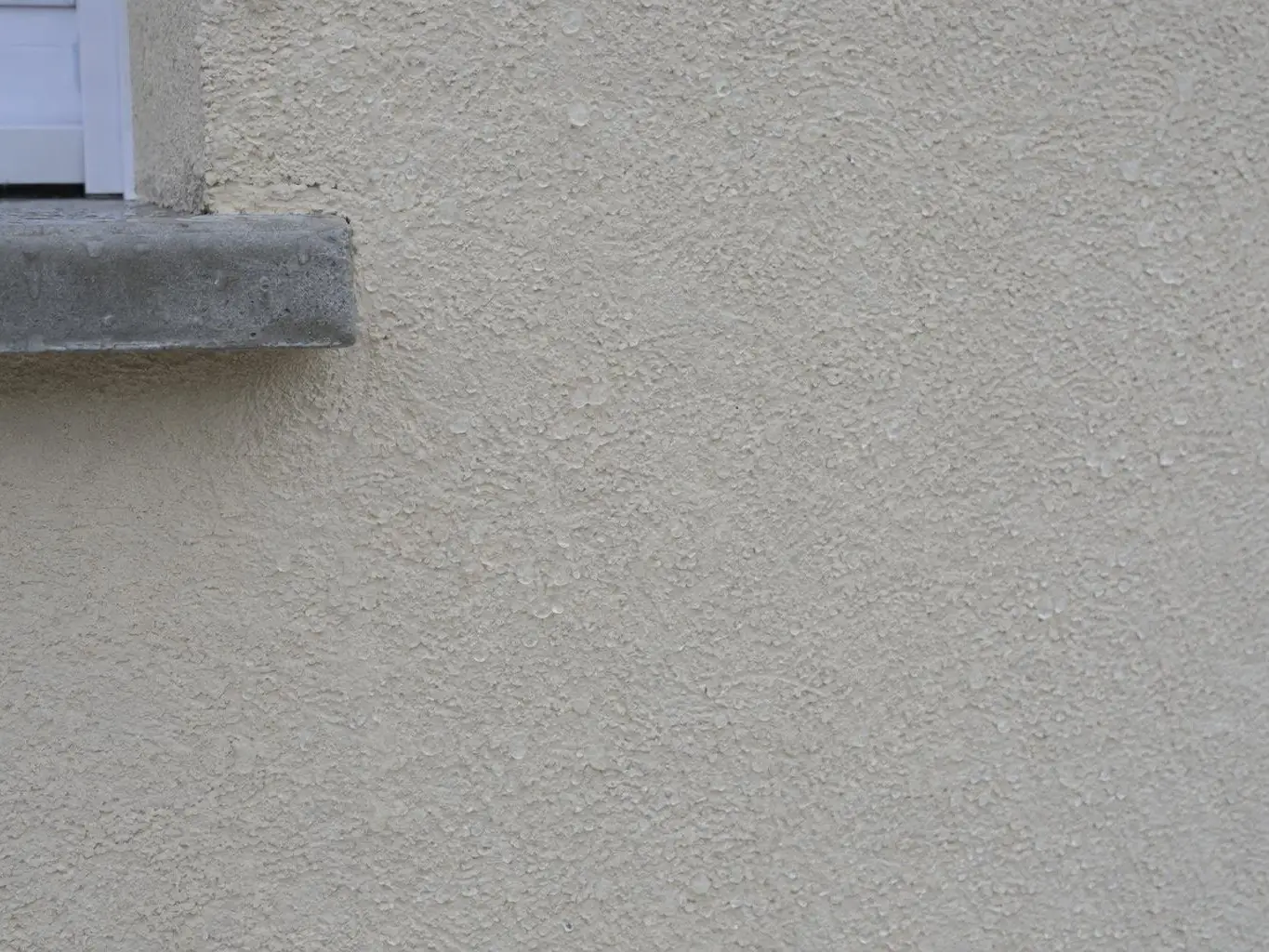 Crépi beige clair propre et de teinte égale sous l’angle d’un appui de fenêtre en béton gris, grain bien net