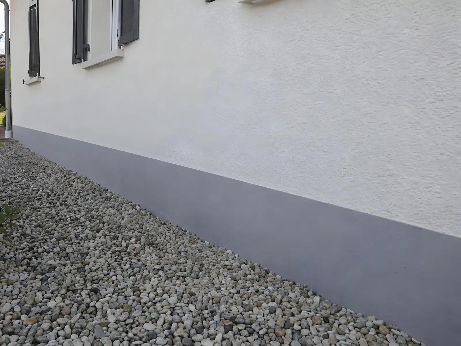 Le même soubassement refait en gris lisse et net le long de la façade blanche et des graviers
