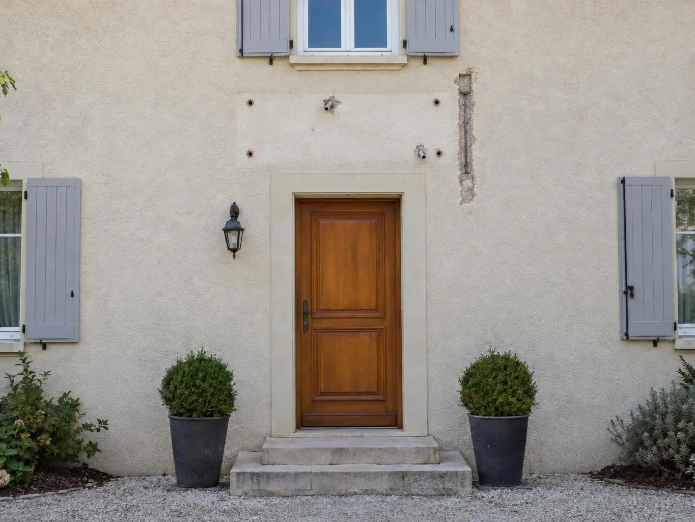 Façade en crépi beige au-dessus d’une porte en bois, empreinte d’auvent démonté avec trous, chevilles et saignée ouverte