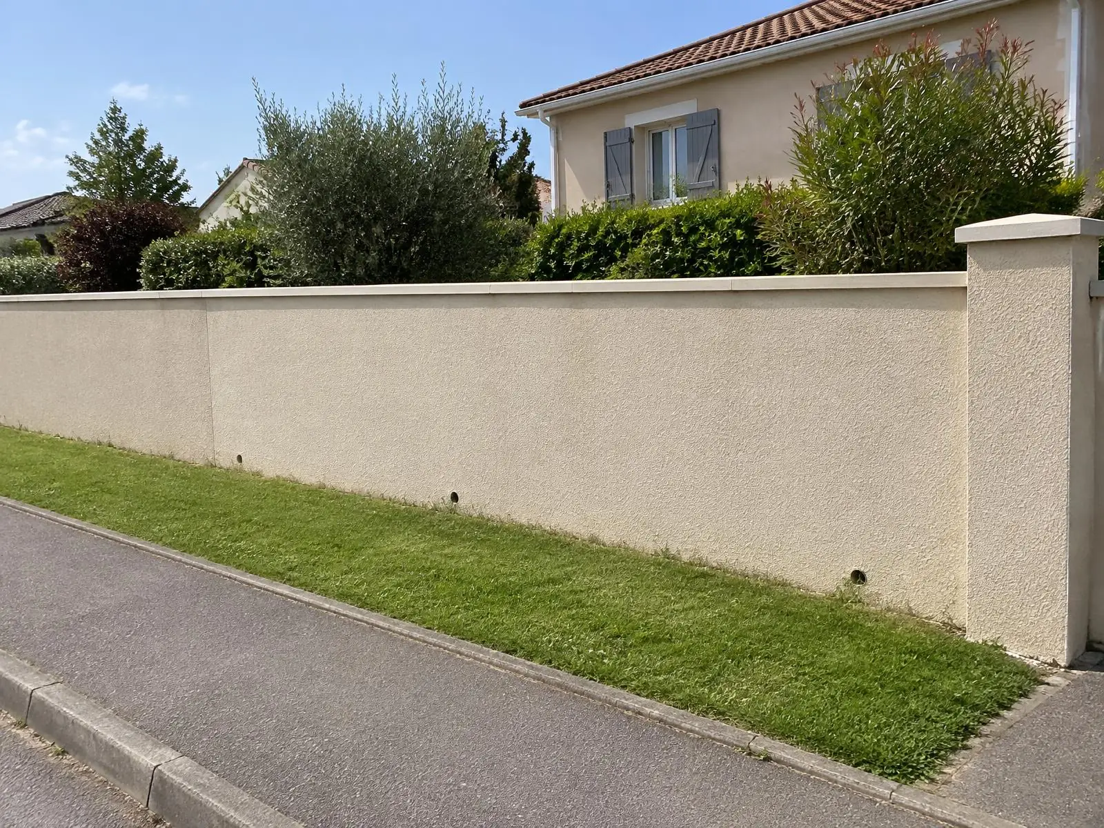 Mur de clôture remonté et enduit beige, chaperon neuf, pilier à chapeau et trous d’écoulement au pied