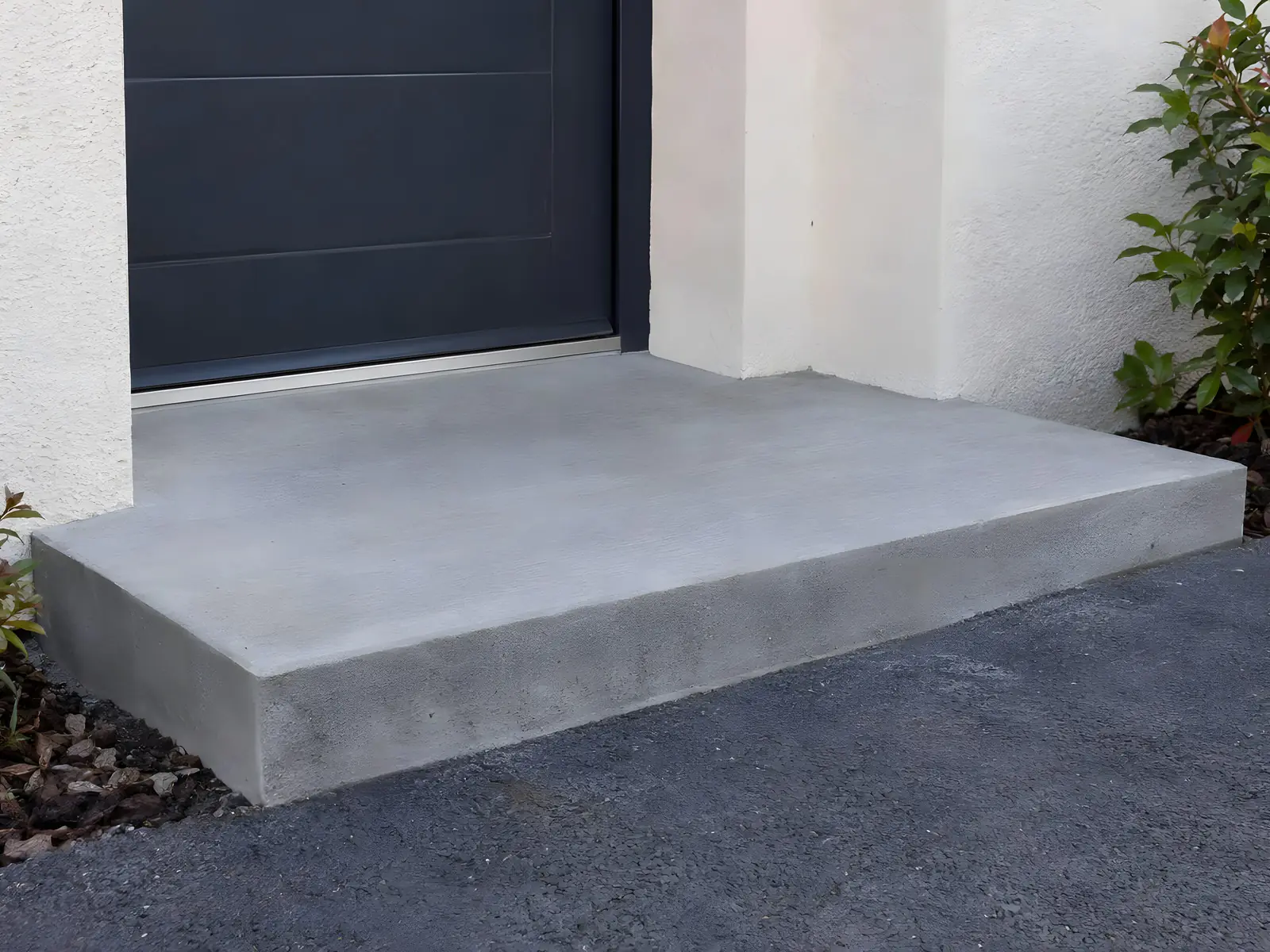 Marche d’entrée en béton lisse et nette, angles droits, au pied d’une porte gris anthracite