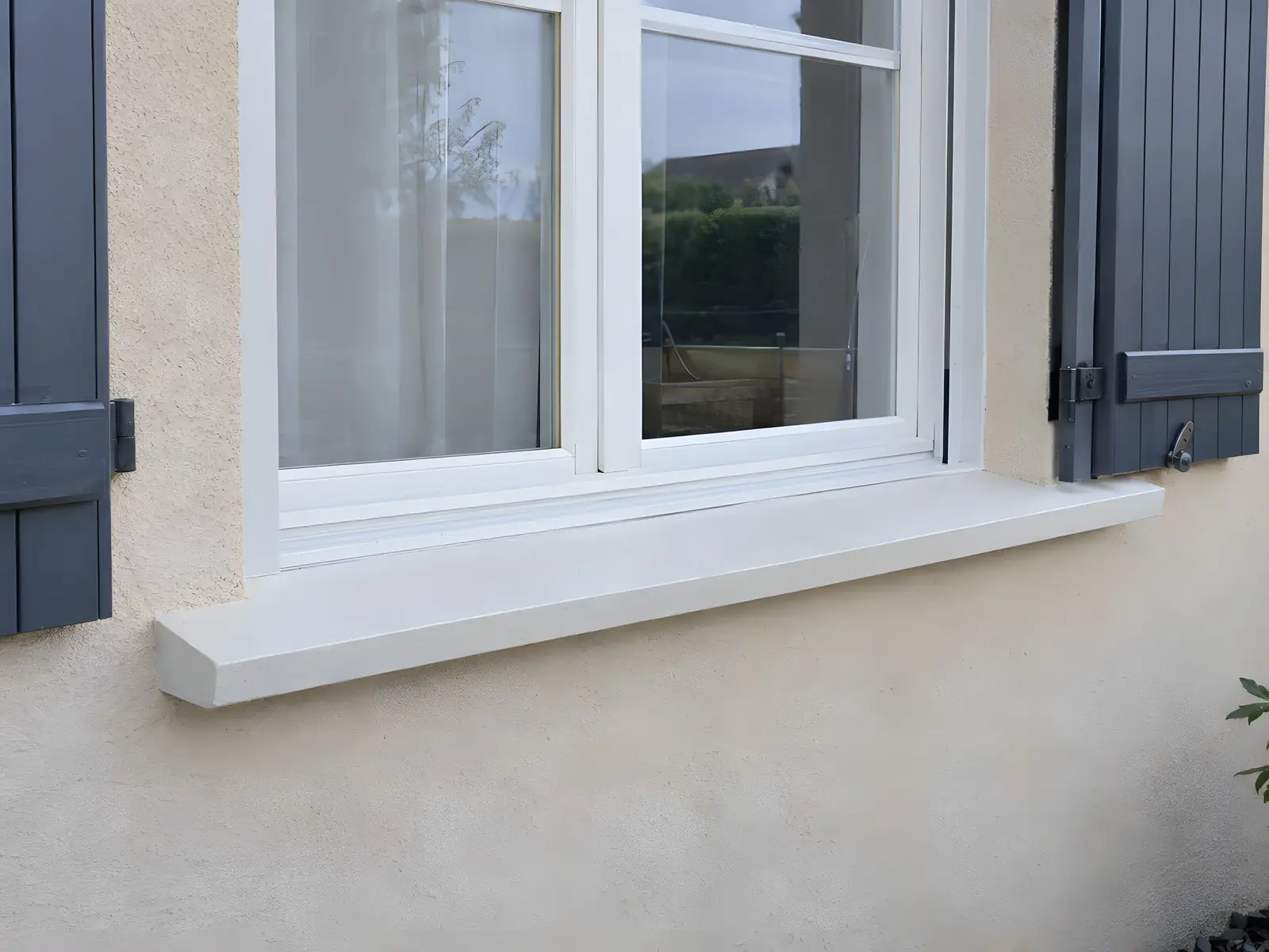 Appui de fenêtre neuf blanc et lisse sous une fenêtre à volets gris, enduit propre en dessous