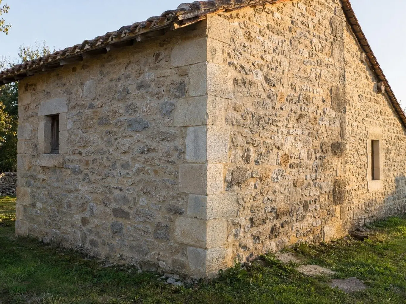 Angle d’une dépendance en pierre au toit de tuiles anciennes, pierres d’angle taillées alignées du sol au toit