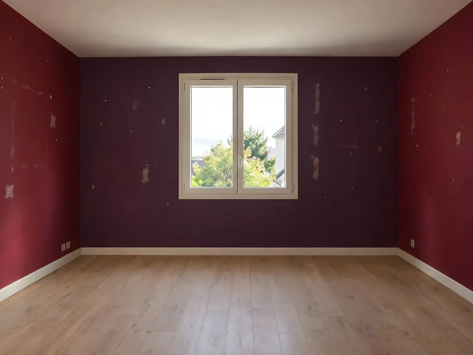 Chambre vide aux murs bordeaux et violet foncé, marqués de traces d’adhésif et de punaises, parquet clair