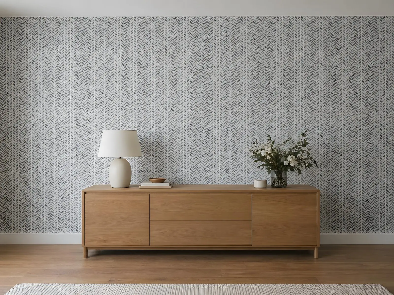 Papier peint intissé à motif chevron gris sur fond blanc derrière un buffet bas en bois, une lampe blanche dessus