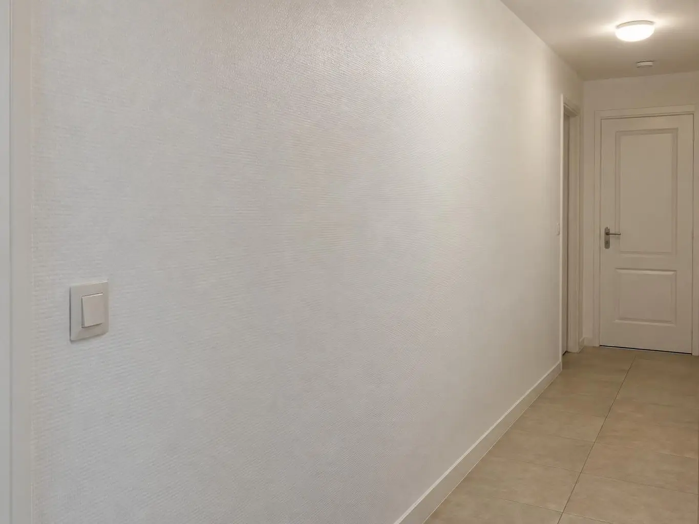 Mur de couloir couvert d’une toile de verre peinte en blanc satiné, trame fine et régulière, porte blanche au fond