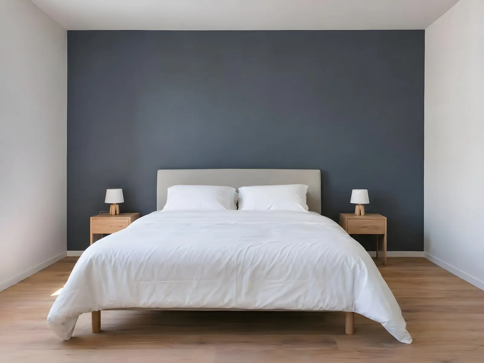Chambre au mur du fond peint en bleu-gris profond derrière un lit blanc, tables de chevet en bois et deux lampes