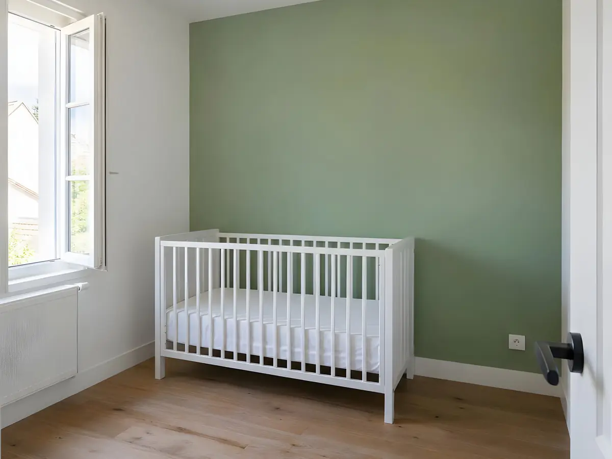 Mur vert d’une chambre d’enfant fraîchement repeint, d’une couleur égale d’un angle à l’autre, lit à barreaux blanc devant
