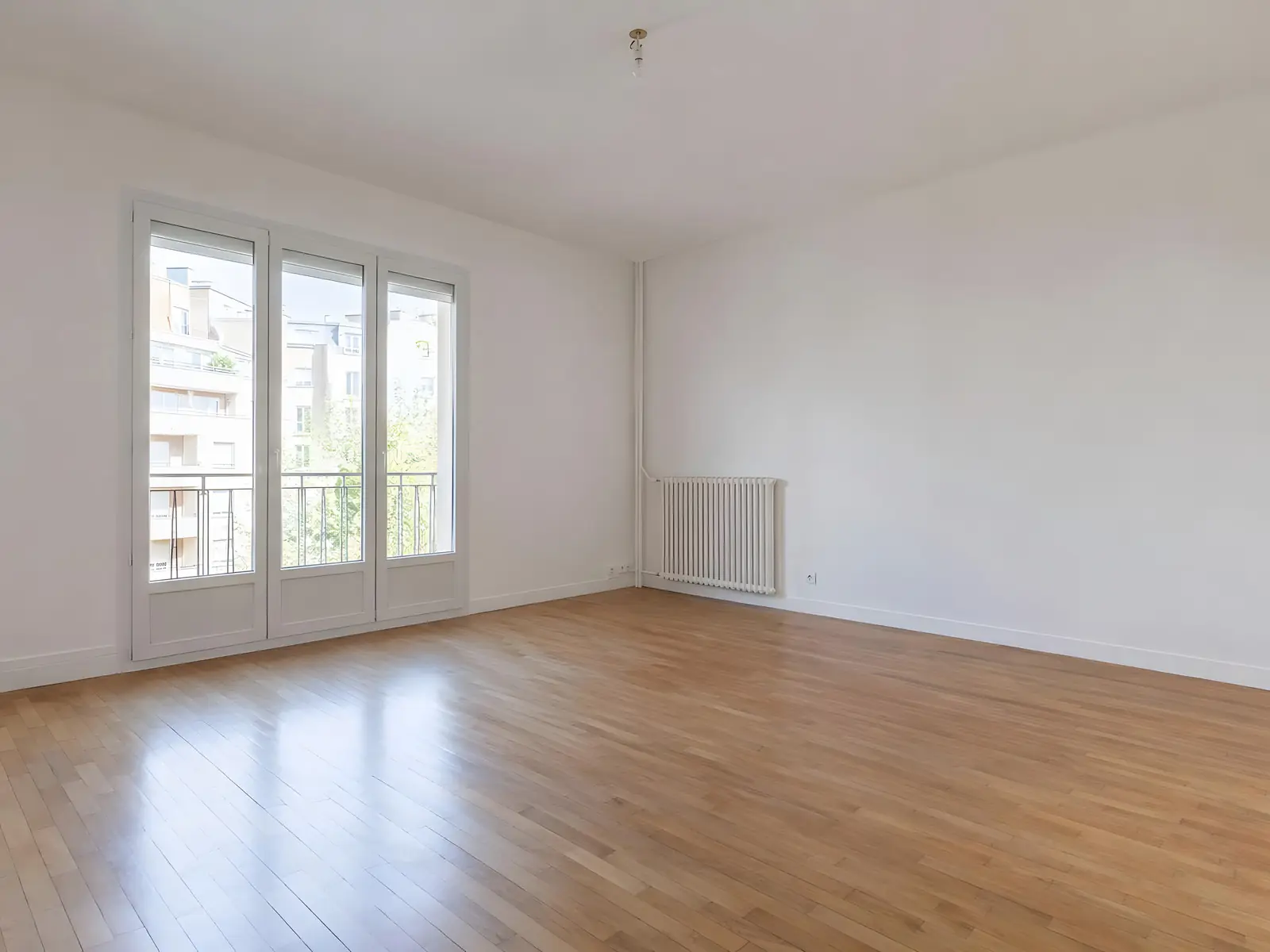 Séjour vide aux murs et au plafond d’un blanc net, grande porte-fenêtre lumineuse et parquet clair