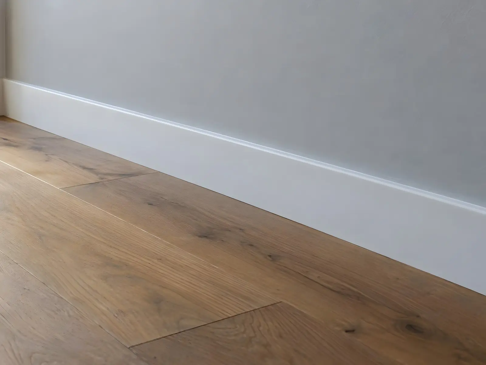 Plinthe laquée blanc satiné, nette et régulière, au pied d’un mur gris clair sur un parquet en chêne intact
