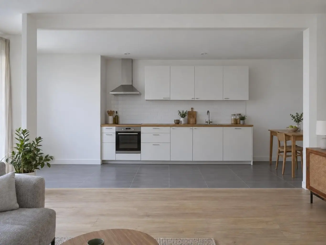 Séjour au parquet clair ouvert sur une cuisine blanche en ligne avec four, hotte inox et petite table