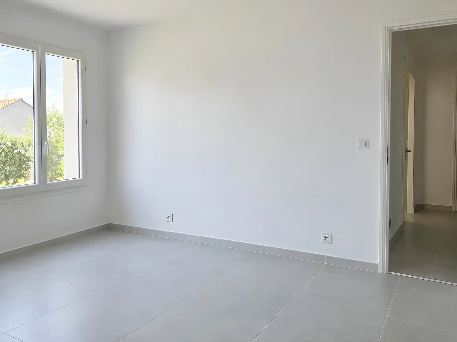 La même pièce aux murs blancs repeints, grand carrelage gris clair au sol et prises encastrées dans le mur