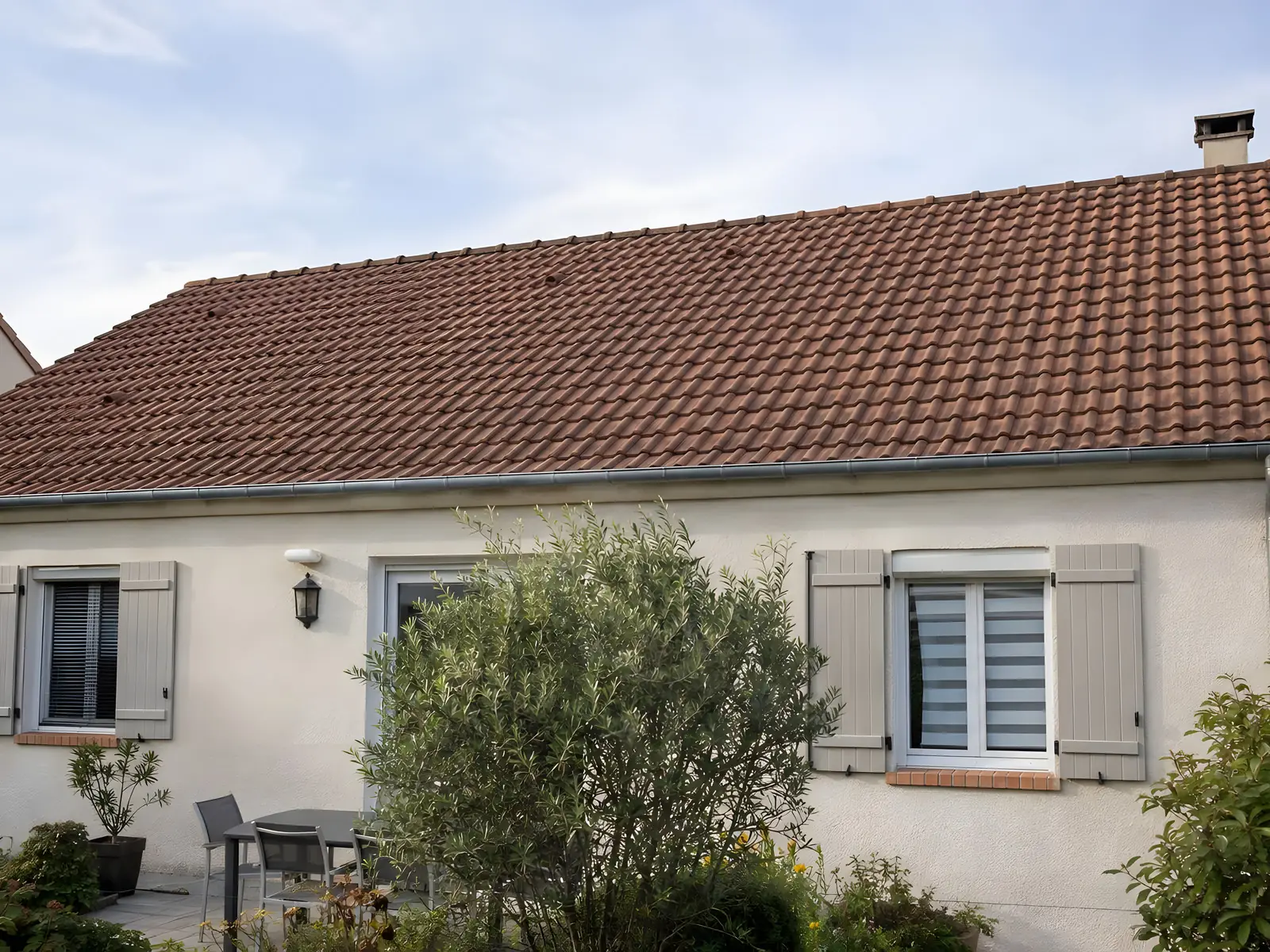 Toit en tuiles rouges d’un pavillon au crépi clair, tuiles nettes et uniformes au-dessus des volets gris