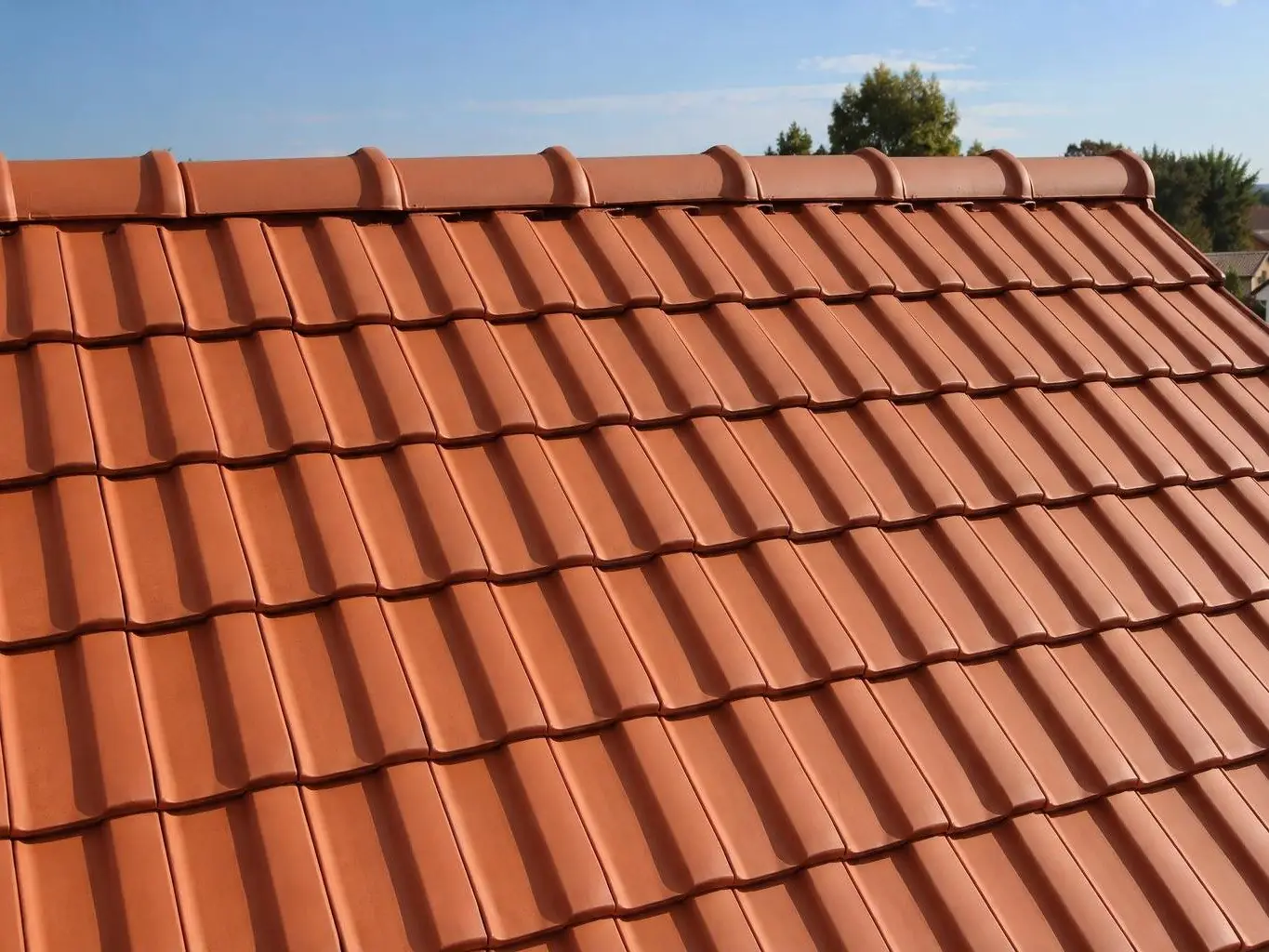 Pan de toit en tuiles mécaniques rouge orangé propres et uniformes, faîtage net sous un ciel bleu