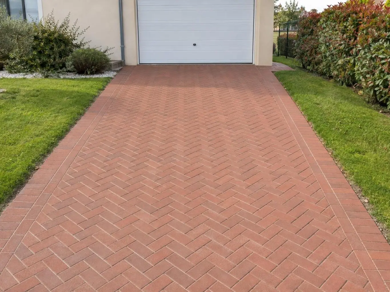 Allée de pavés ocre rouge en chevrons, couleur vive, joints nets, menant à une porte de garage blanche